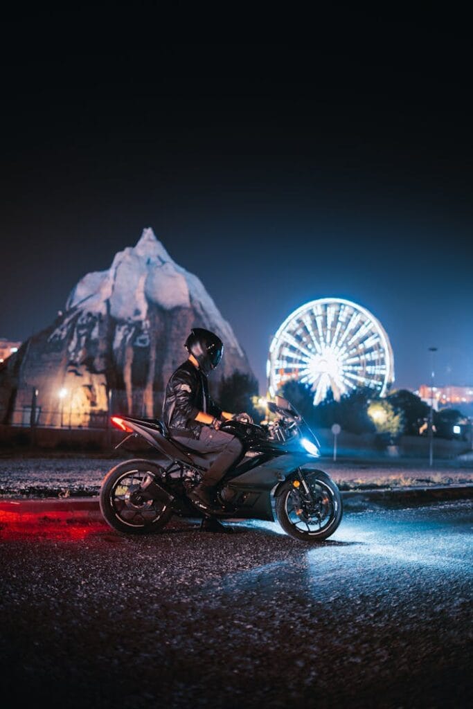 A motorcyclist captured at night in front of an illuminated ferris wheel, creating a vibrant nightlife scene.